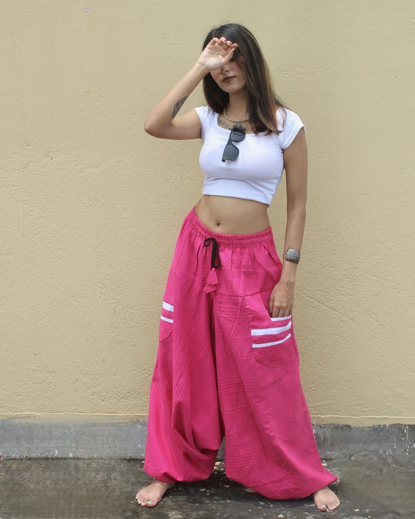 Person wearing a white crop top and pink wide-leg harem pants with a beige wall background
