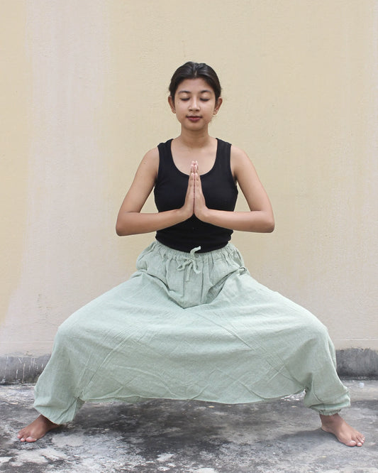Person in a yoga pose with a plain background wearing harem pants