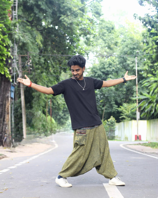 Person standing with arms outstretched on a road surrounded by greenery wearing harem pants