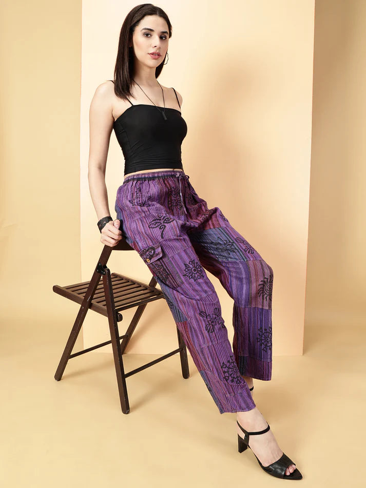 Woman wearing a black top and purple patterned pants sitting on a chair against a beige background
