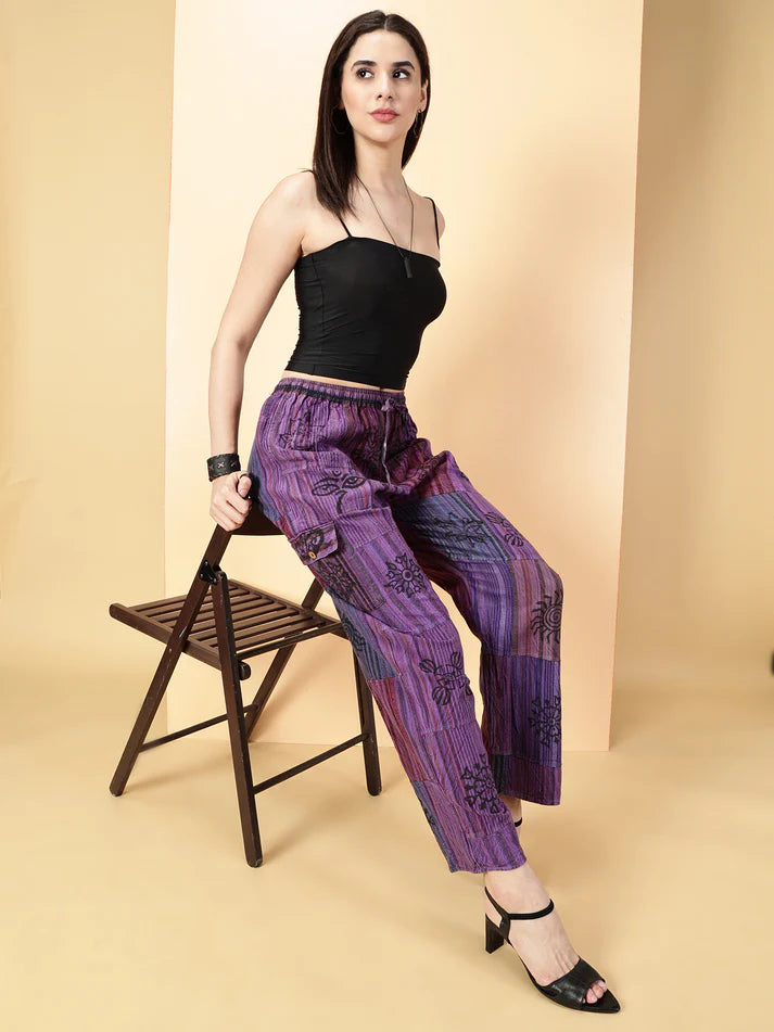 Woman wearing a black top and purple patterned pants sitting on a chair against a beige background