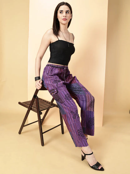 Woman wearing a black top and purple patterned pants sitting on a chair against a beige background