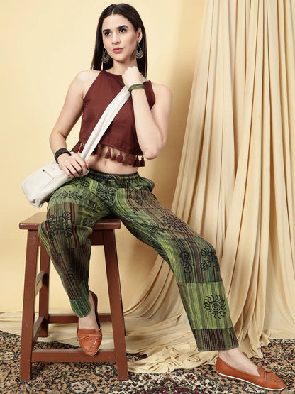 Woman sitting on a stool wearing a maroon top and green patterned pants, holding a white bag.