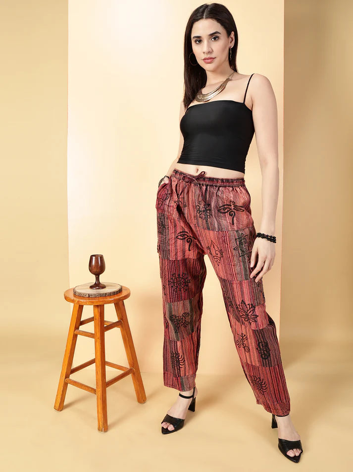 Woman wearing a black top and red patterned pants standing next to a wooden stool on a beige background