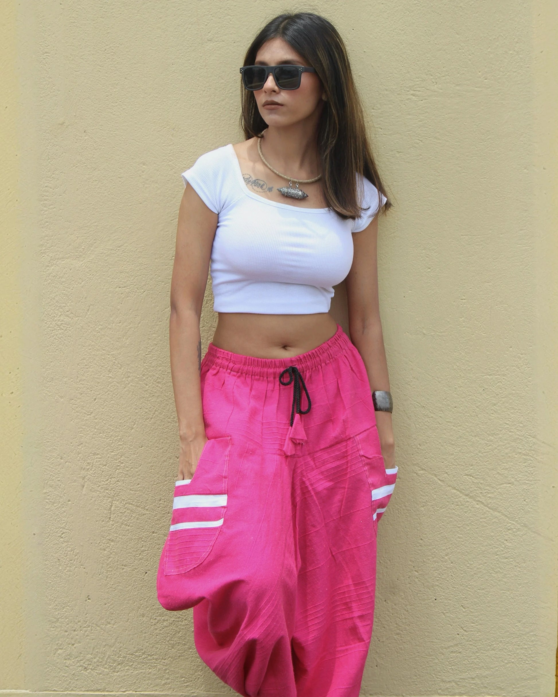 Woman wearing a white crop top and pink harem pants with white stripes against a beige wall.