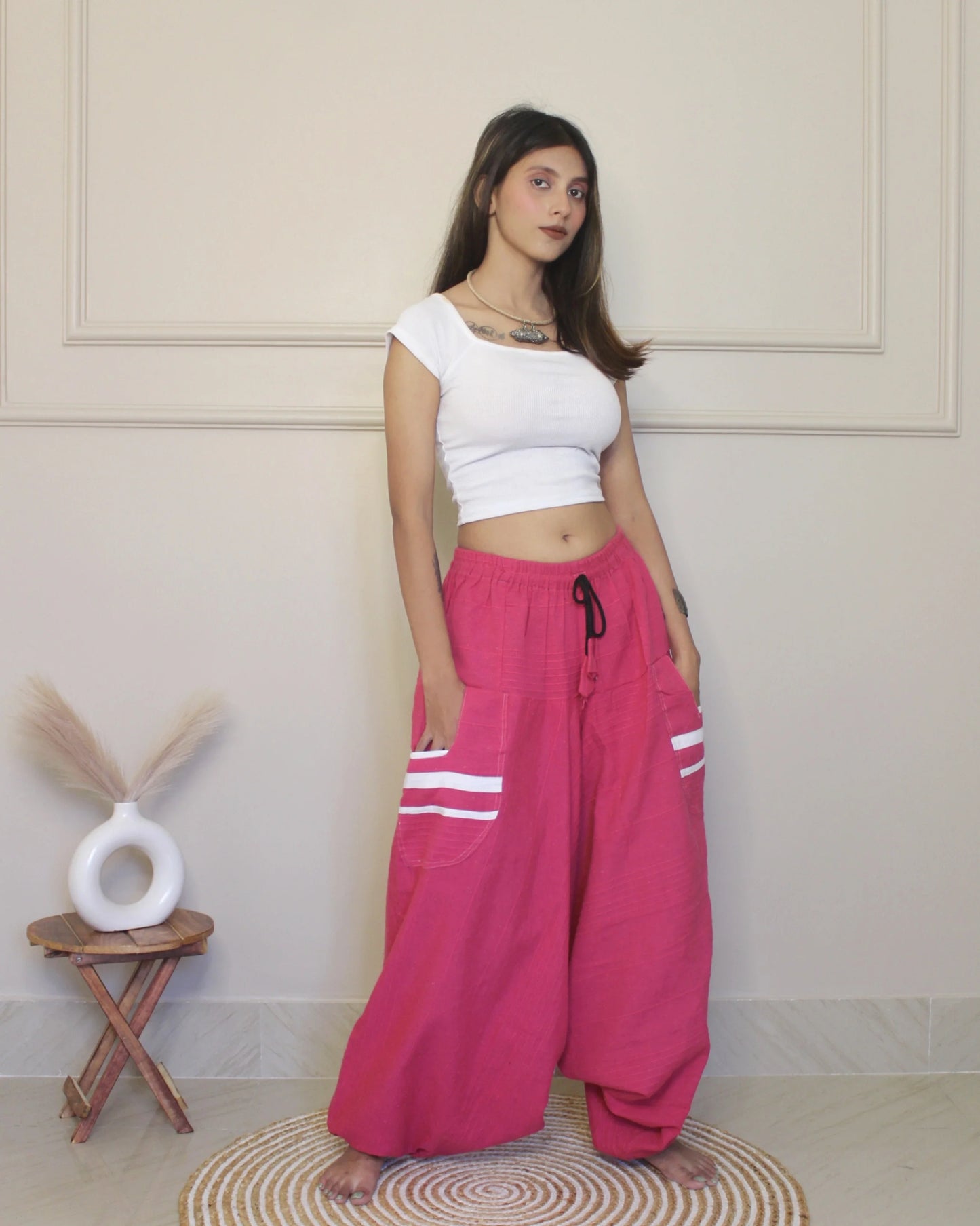 Woman wearing a white top and pink harem pants with white stripes indoors.