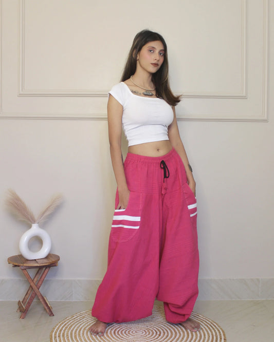 Woman wearing a white top and pink harem pants with white stripes indoors.