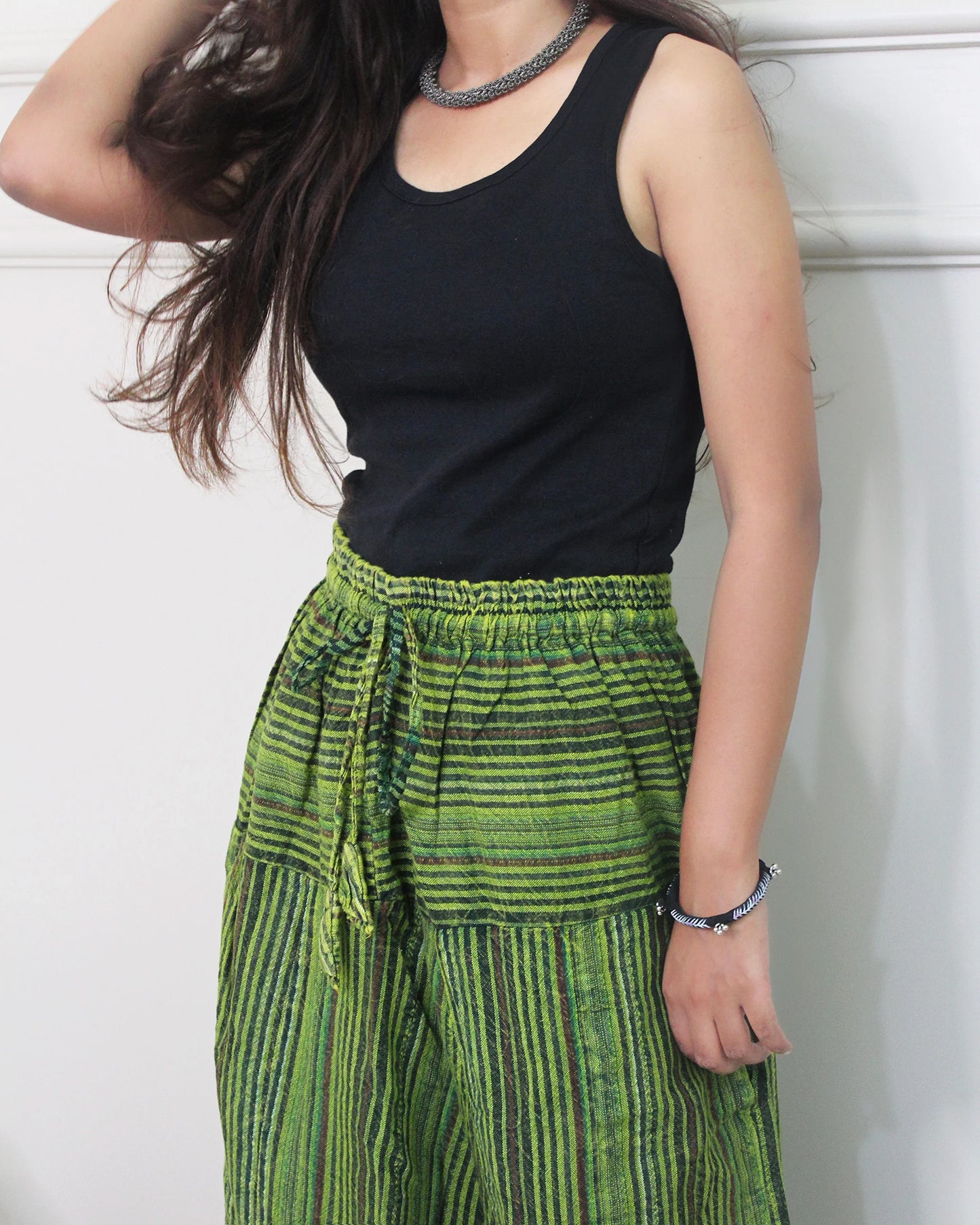Person wearing a black tank top and green striped harem pants against a white background