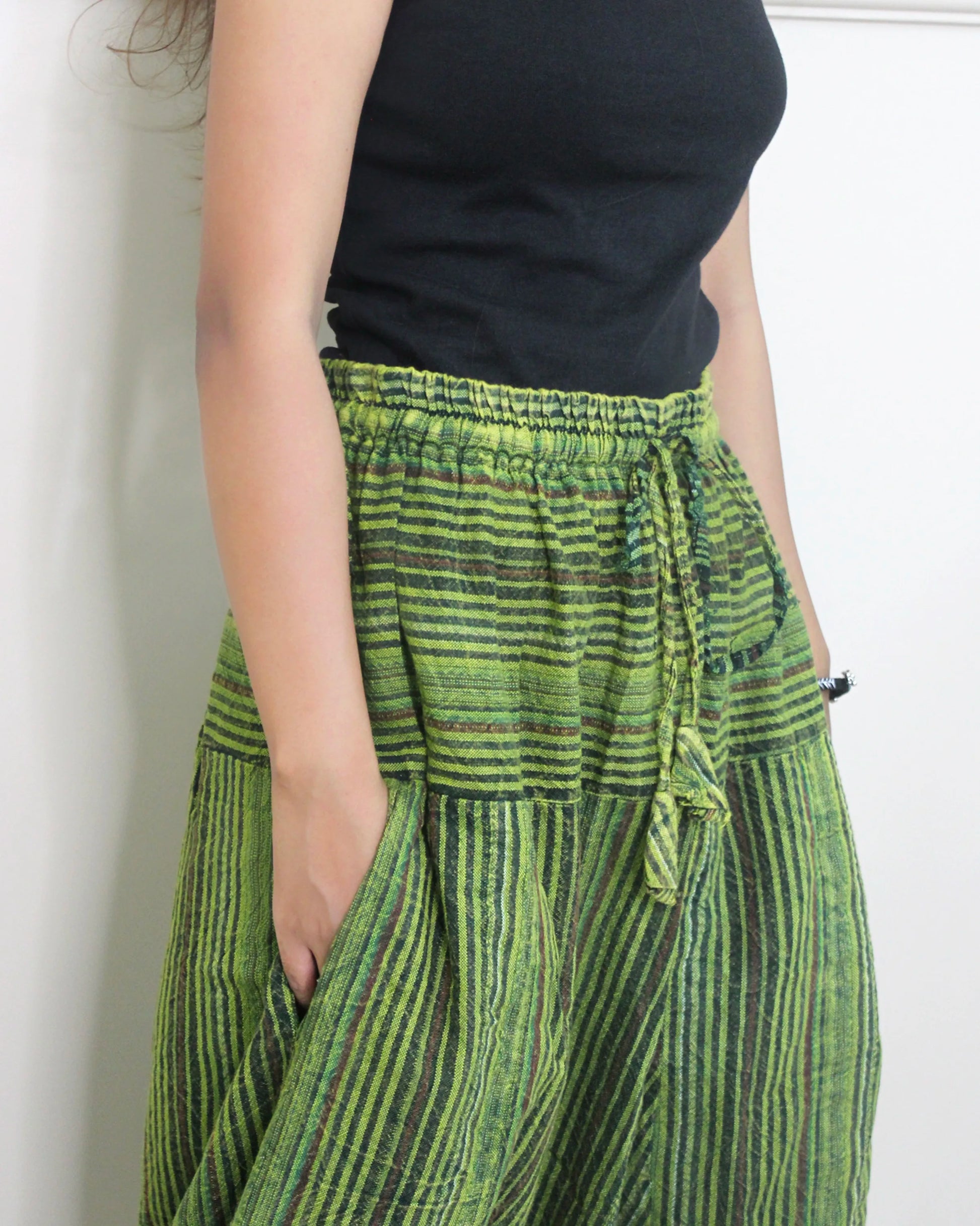 Person wearing a black top and green striped harem pants against a white background