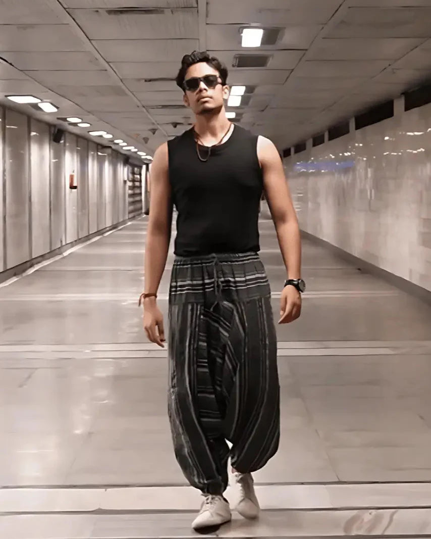 Man wearing harem pants and a black tank top in a long, narrow hallway.