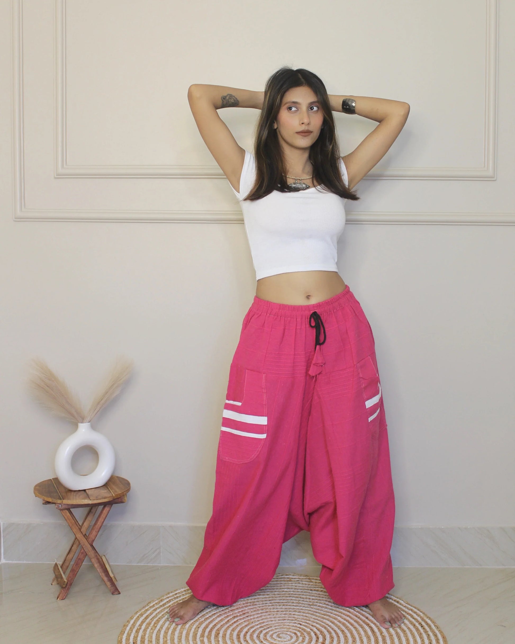 Woman wearing a white crop top and pink harem pants with white stripes indoors.