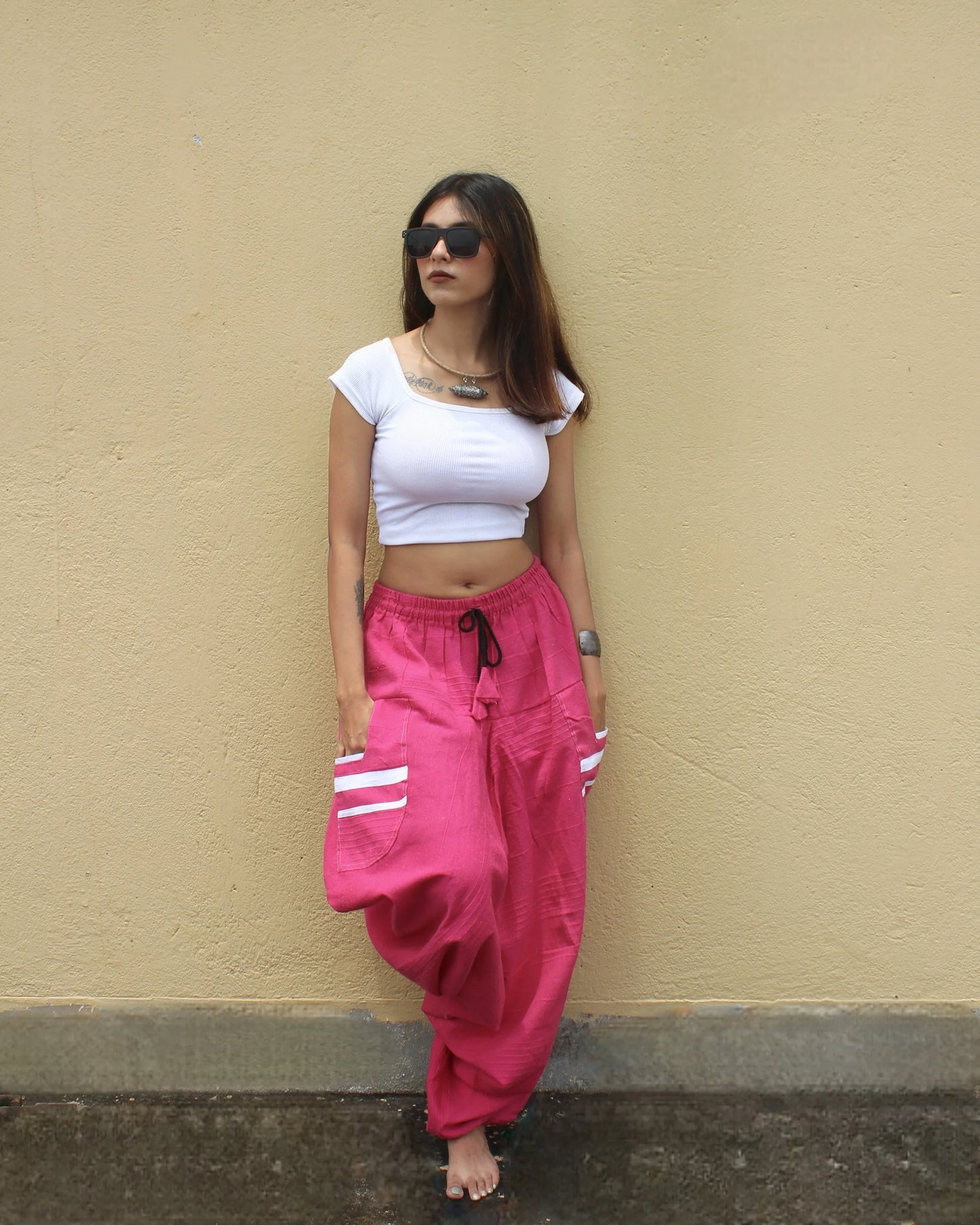 Woman wearing a white crop top and pink harem pants against a beige wall.