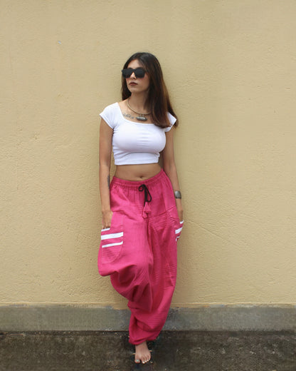 Woman wearing a white crop top and pink harem pants against a beige wall.