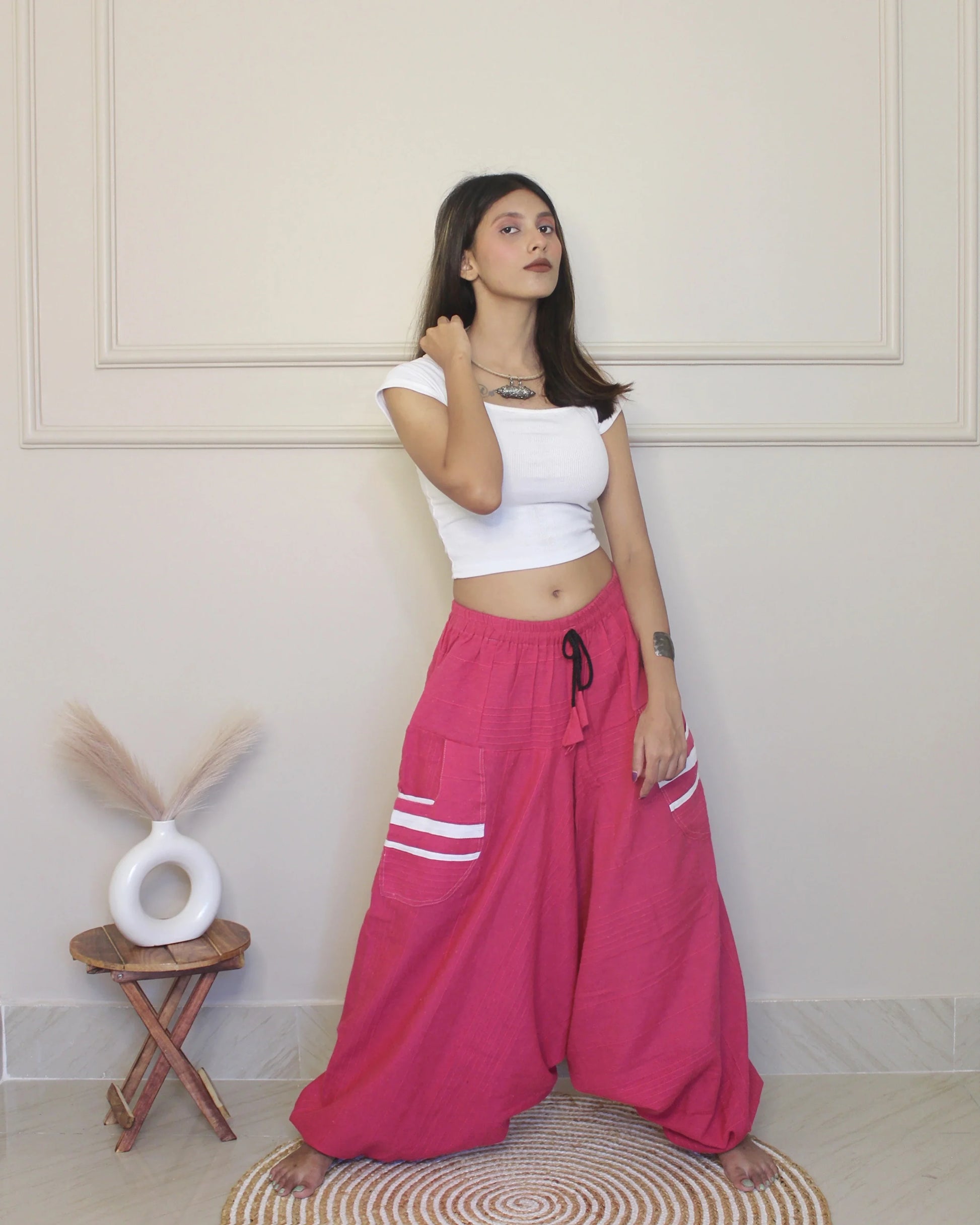 Woman wearing a white top and pink harem pants with white stripes indoors.