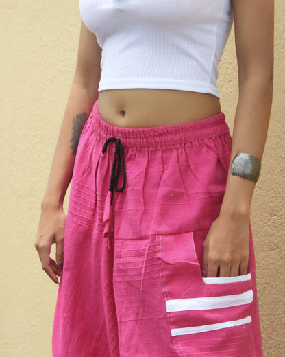 Person wearing a white crop top and pink harem pants with white stripes on a beige background