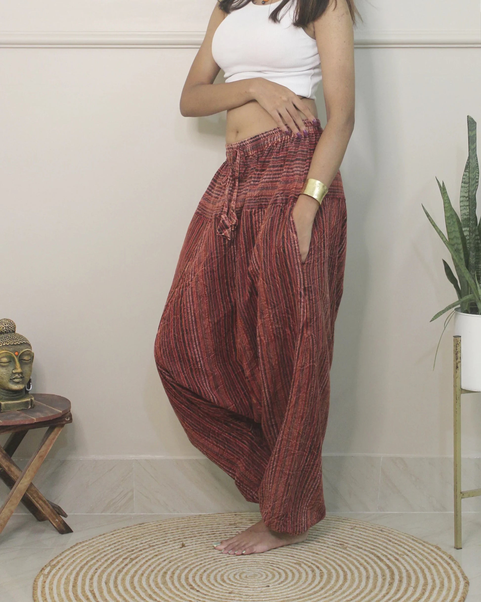 Person wearing red harem pants standing in a room with a Buddha statue and plant.