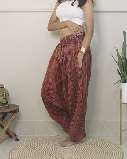 Person wearing red harem pants standing in a room with a Buddha statue and plant.