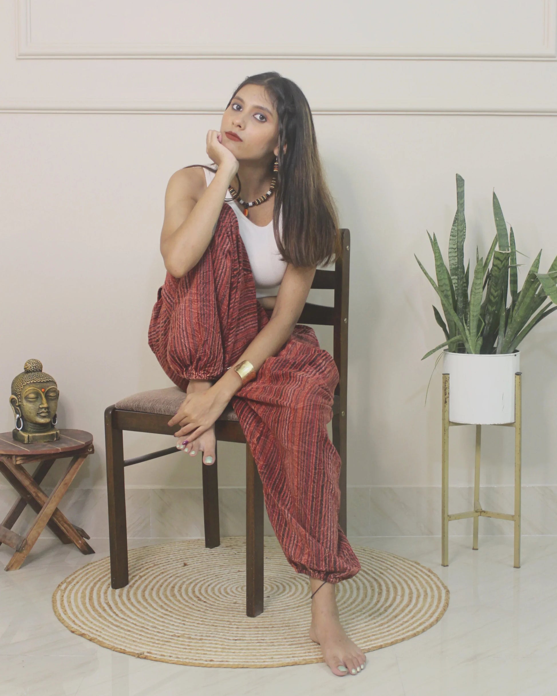 Woman sitting on a chair wearing harem pants in a room with a plant and small table.