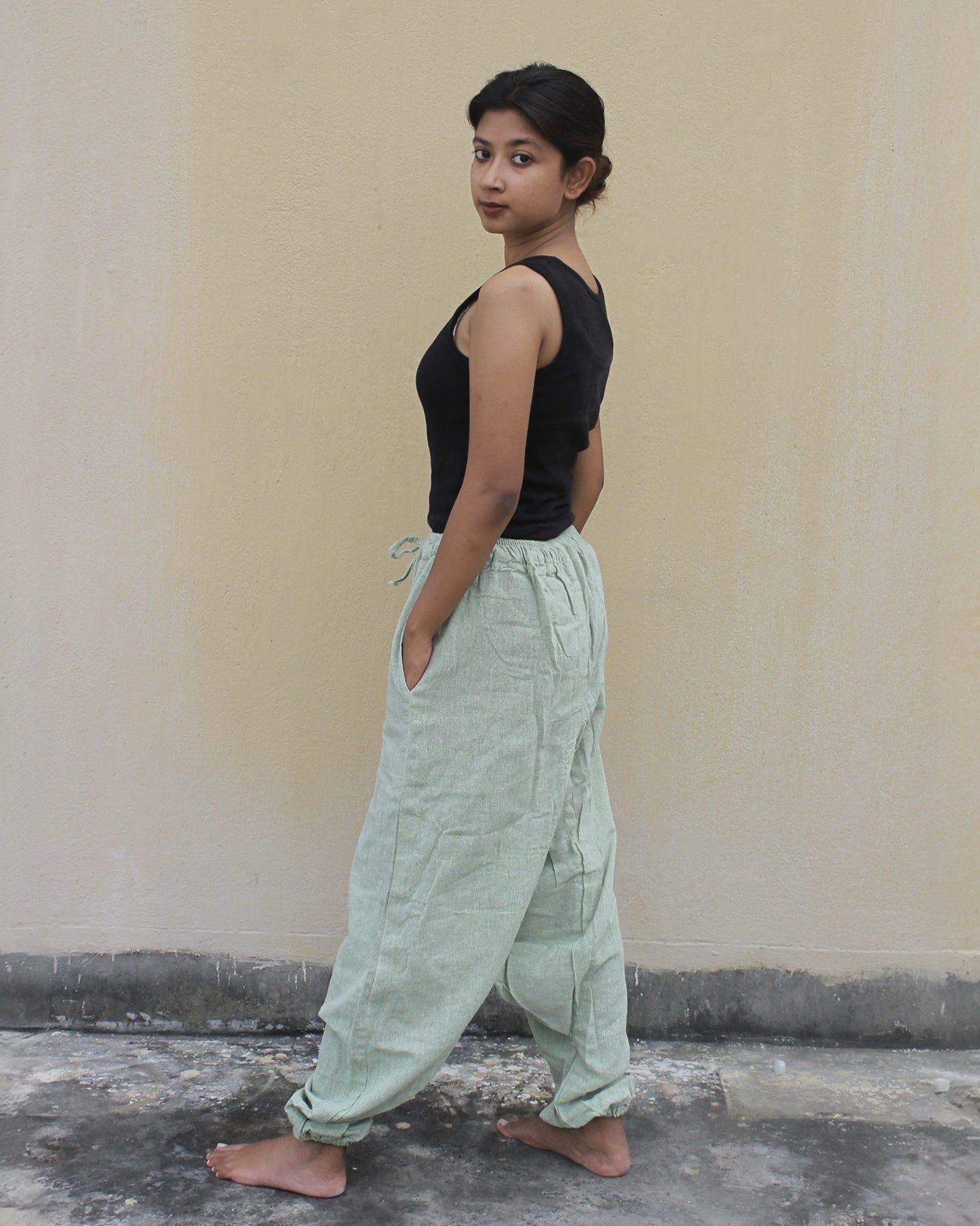 Person wearing a black top and light green harem pants against a plain wall.