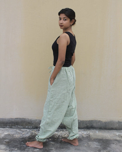 Person wearing a black top and light green harem pants against a plain wall.