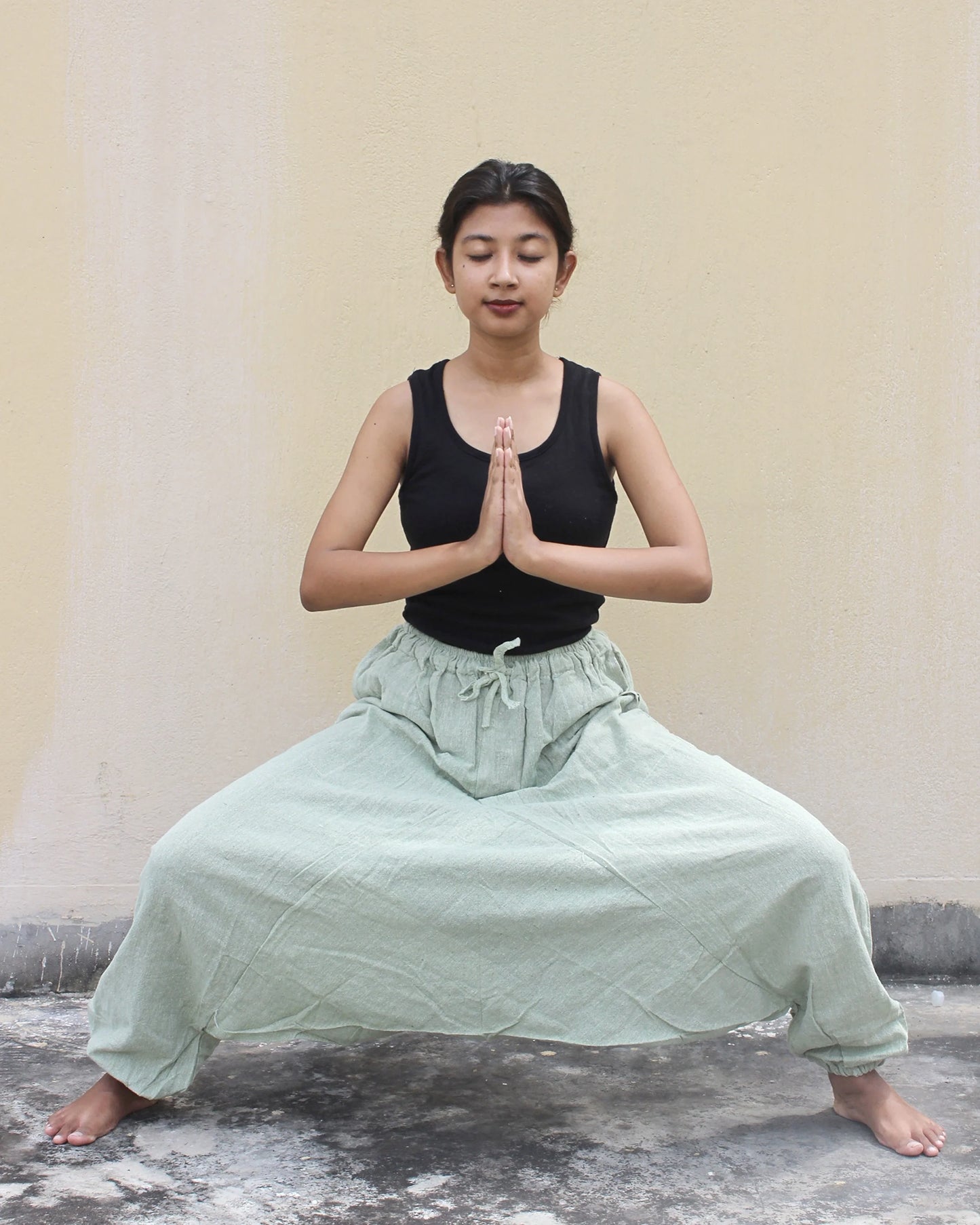 Person in a yoga pose with a plain background wearing harem pants