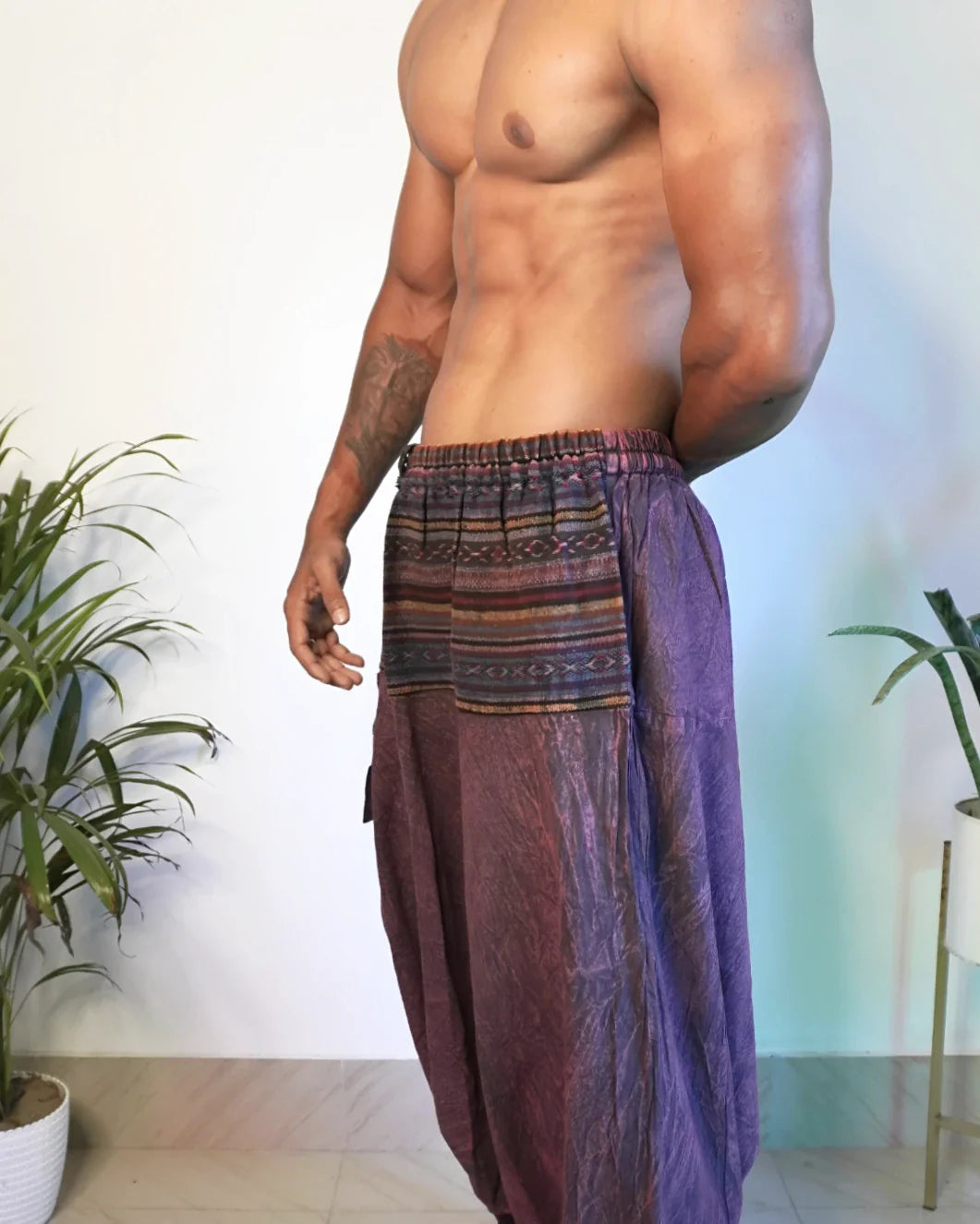 Man wearing a colorful, patterned harem pants in an indoor setting with plants.
