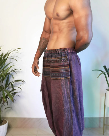 Man wearing a colorful, patterned harem pants in an indoor setting with plants.