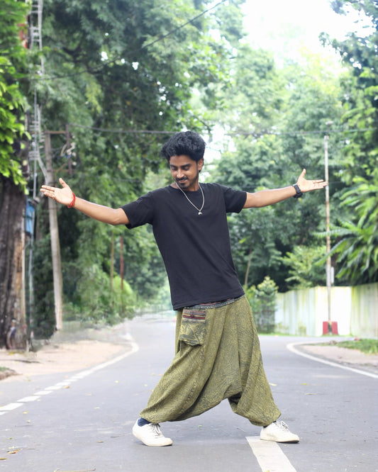 Person standing with arms outstretched on a road surrounded by greenery wearing harem pants