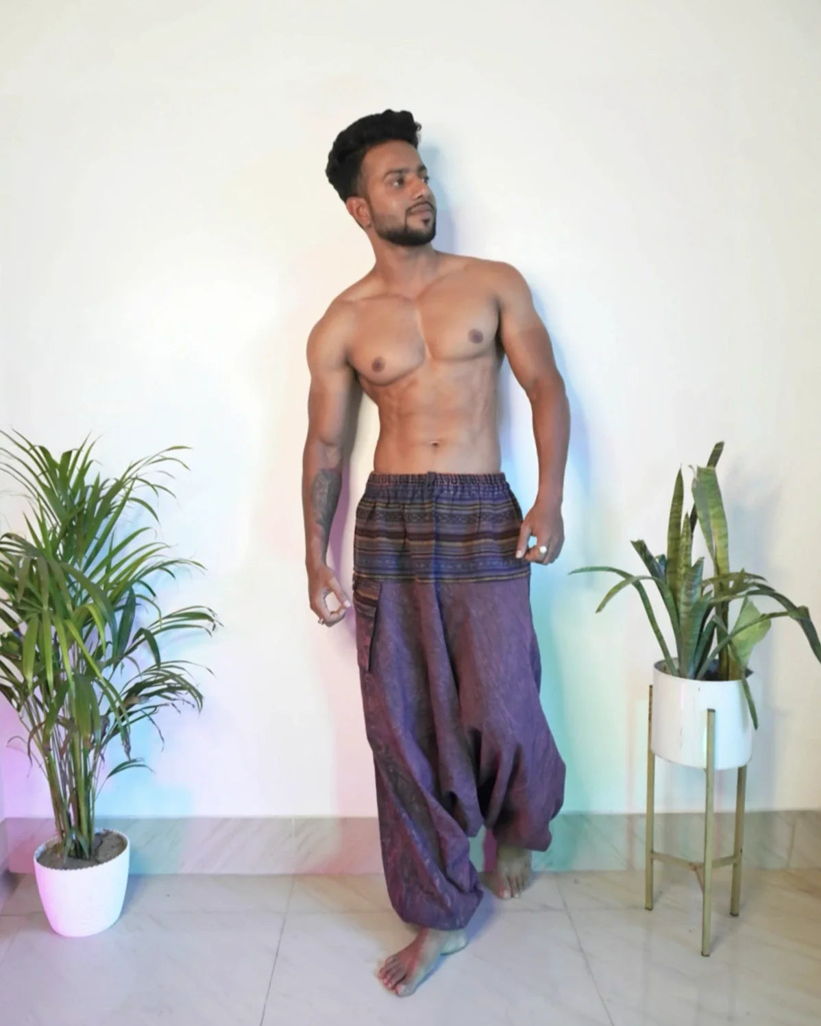 Man wearing purple harem pants standing in a room with plants.