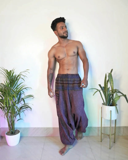 Man wearing purple harem pants standing in a room with plants.