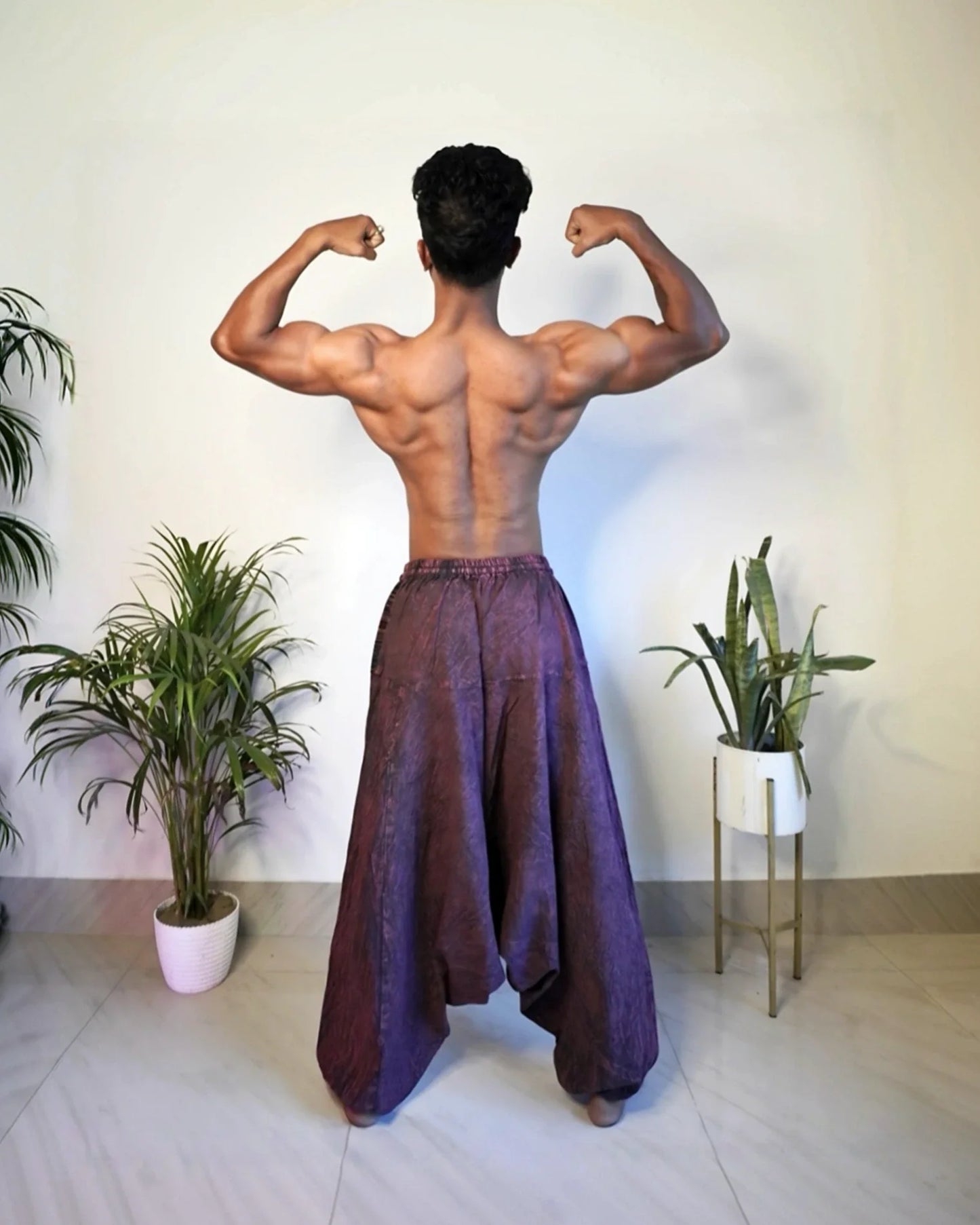 Person flexing muscles in wide-leg harem pants with indoor plants in the background