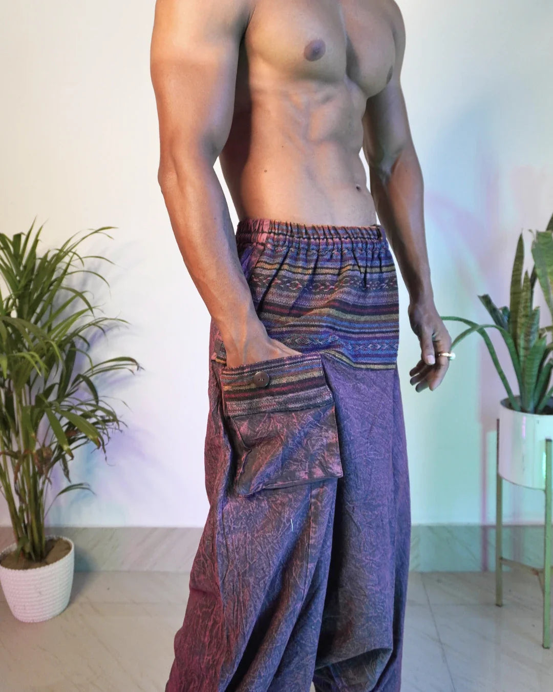 Person wearing colorful harem pants standing indoors with plants in the background