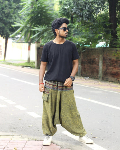 Man wearing a black t-shirt and green baggy harem pants standing on a street.
