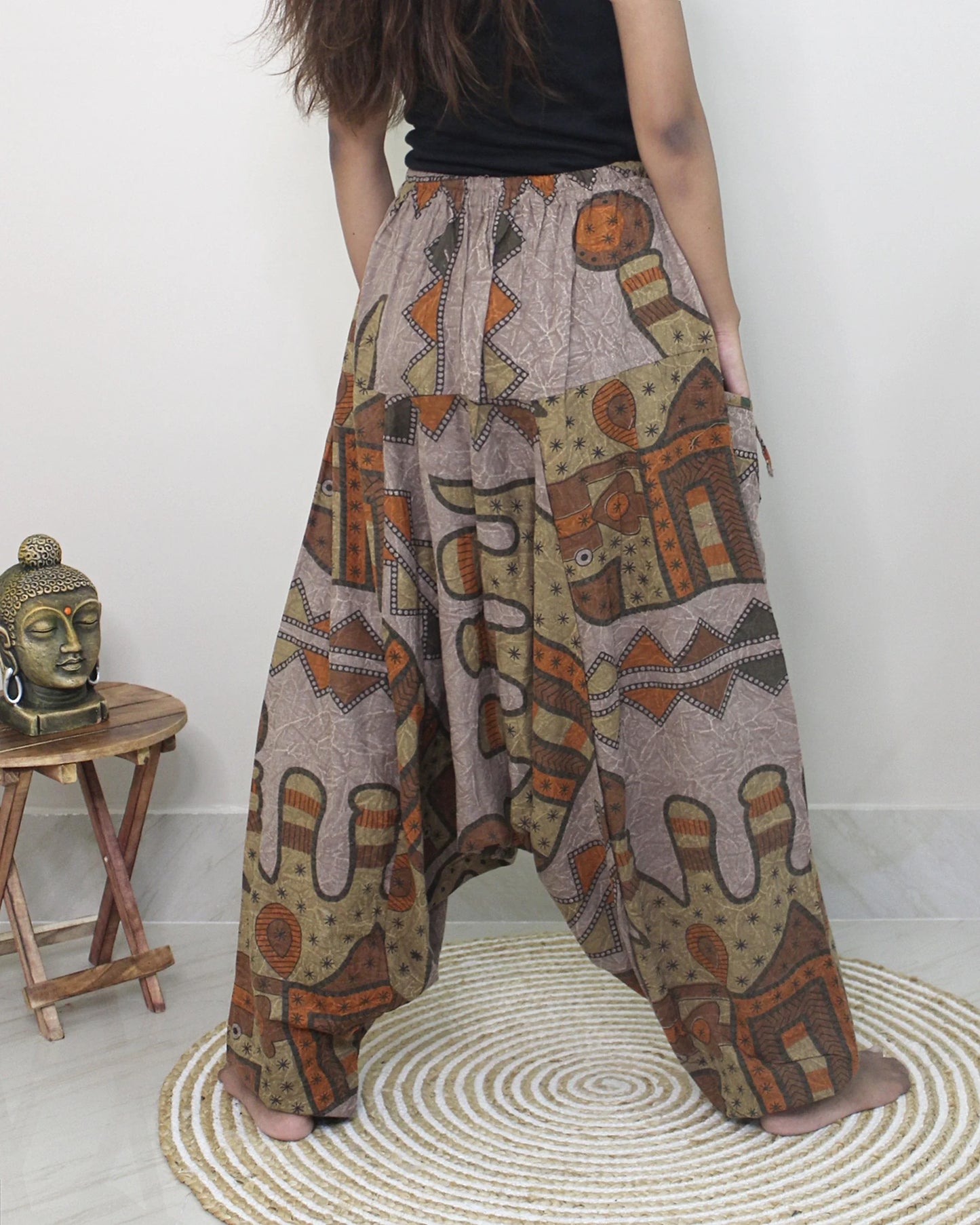 Person wearing patterned wide-leg harem pants with a small wooden table and decorative item in the background.