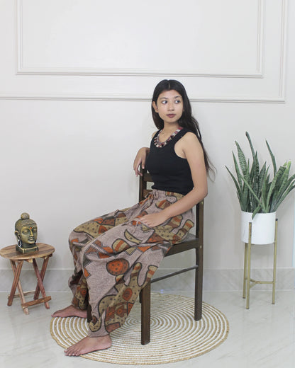 Woman sitting on a chair wearing a black top and patterned harem pants in a minimalistic room.