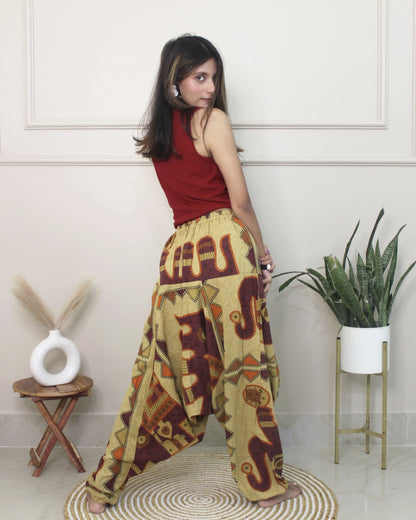 Woman wearing a red top and patterned harem pants in a room with a plant and small table.